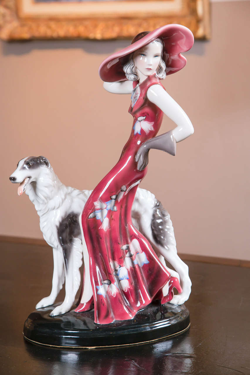 A Goldscheider porcelain Deco woman in red with Russian wolfhound or Borzoi. 
Larger of the two sizes made. Black back stand marked 