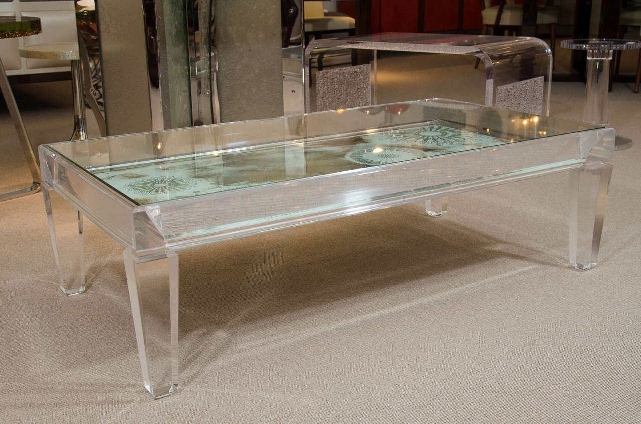 Rectangular Lucite table with chunky tapered legs, inset glass top and stenciled reverse painted mirror interior decoration.