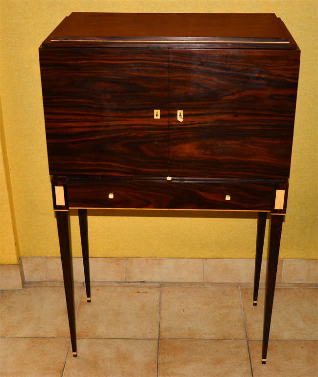 Small 1930-1040 cabinet in solid rosewood; legs have boxwood inlay; eight interior drawers and one pull out tablet in parchment; large drawer at lower level.