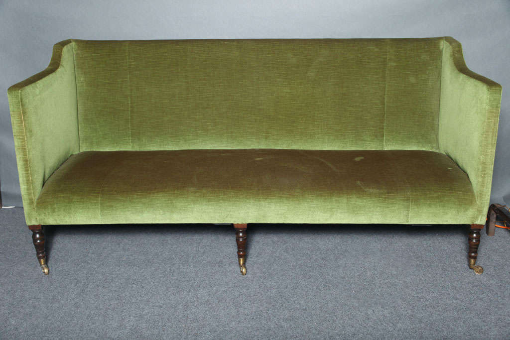 An unusual and beautiful 18th century English Regency sofa with modernist lines, having narrow arms and back, the arms slightly stepped, standing on six turned legs on original brass castors, the whole having very tailored lines.  This sofa offers