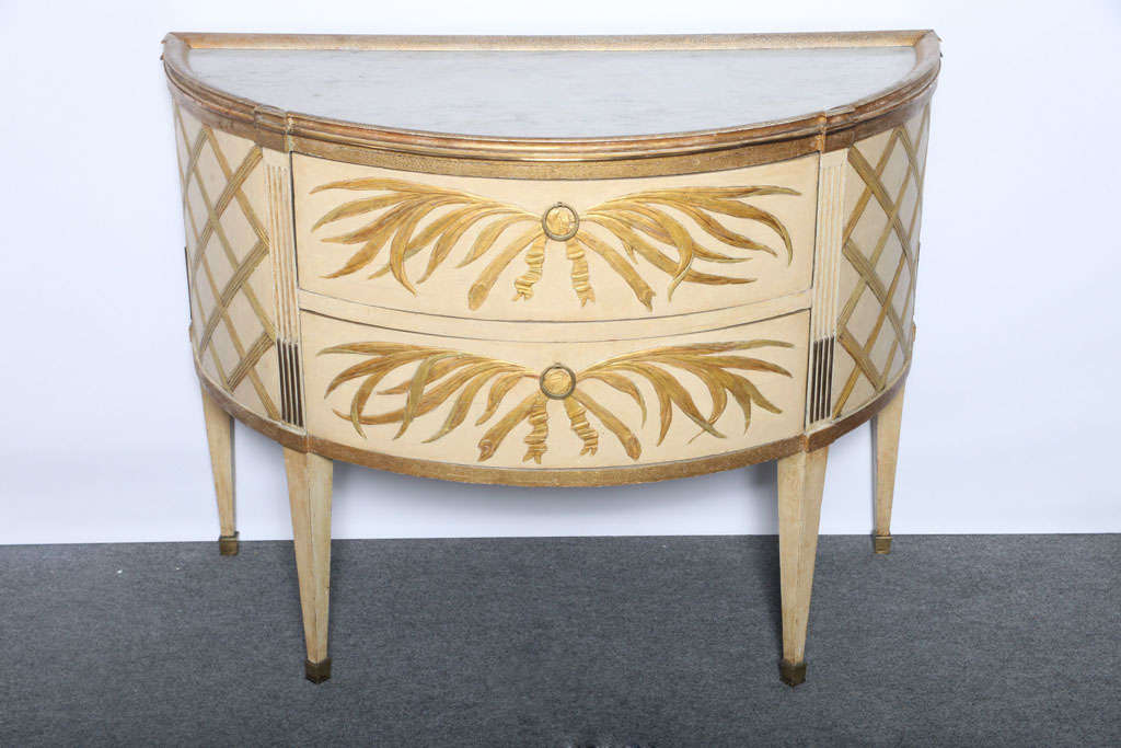Unique pair of painted and gilt commodes, the demilune marble tops surmounted with giltwood molded framed having a punched ground, over two drawers with crossed palm branches tied with a ribbon, stop fluted upper leg with giltwood flutes and bronze