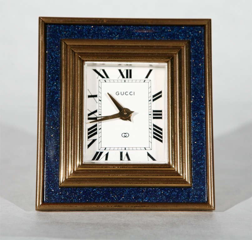 This remarkable brass and lapis enamel desk clock by Gucci with its Roman numeral dial is congruent to the Art Deco style.  It requires winding every 8 days and each windup key is detailed with a small sapphire jewel.  This piece also features an