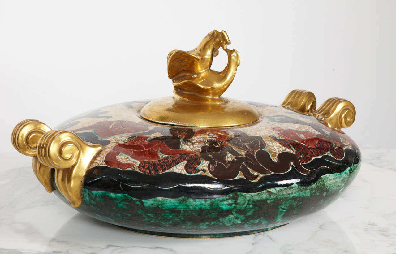 Jean Mayodon (1893-1967)
Circular table centerpiece
Polychrome ceramic: green, red, beige and black. Decorated with anthropomorphic creatures with animal heads. Golden, scroll-shaped handles. Golden top decorated with a rooster and a hen.
Signed