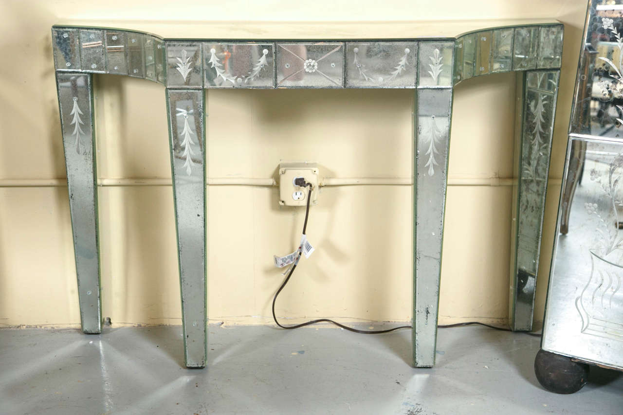 Pair of etched antiqued glass Hollywood Regency mirrored consoles. This fine pair of antiques beveled glass mirrored consoles having tapering legs with etched design supporting a top with a 19 panel beveled glass and etched design apron under an