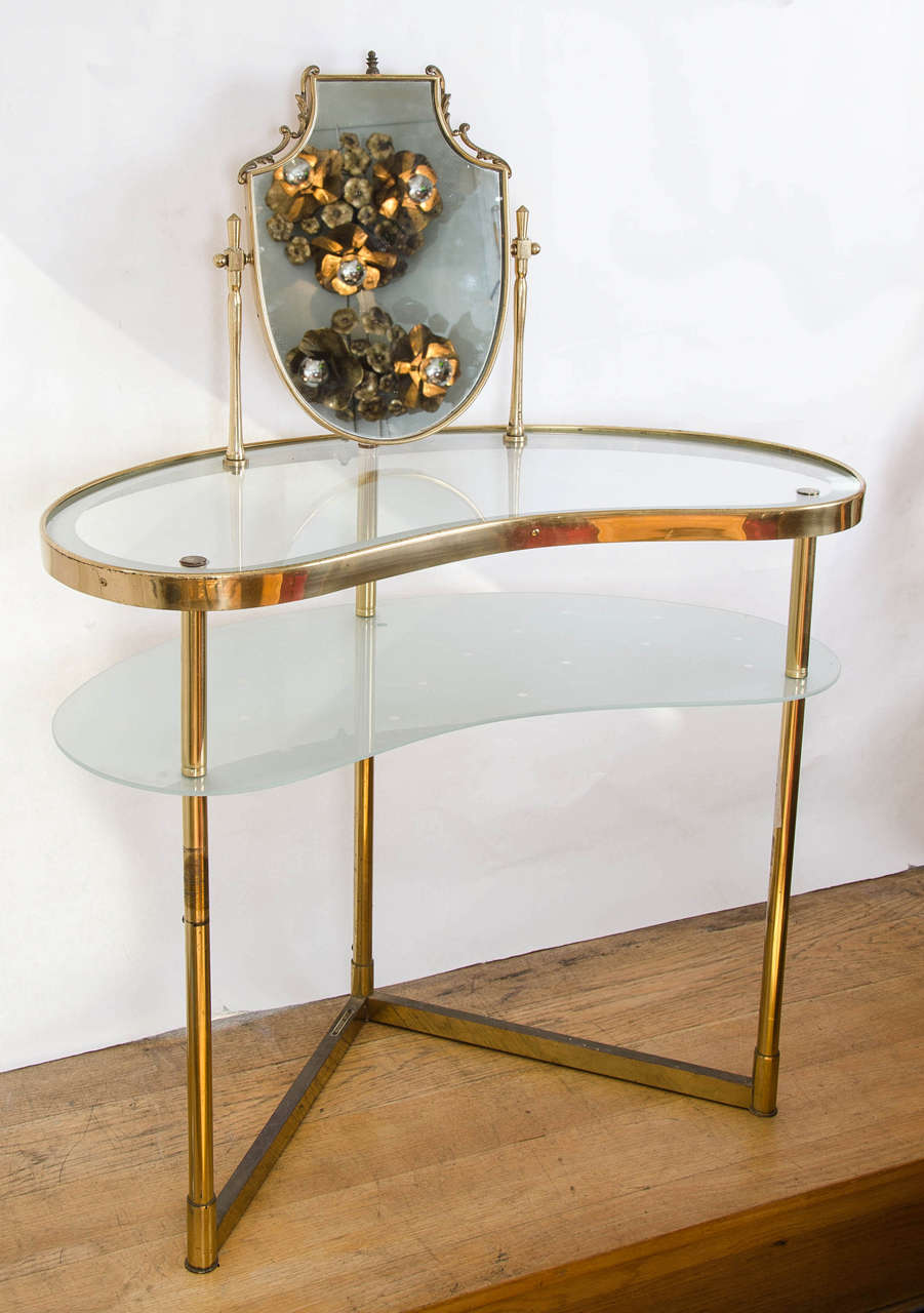 Two-tiered, 1950s brass dressing table with integral decorative shaped mirror, the lower shelf glass shelf etched with a polka dot design and with switch operating a fitted light.