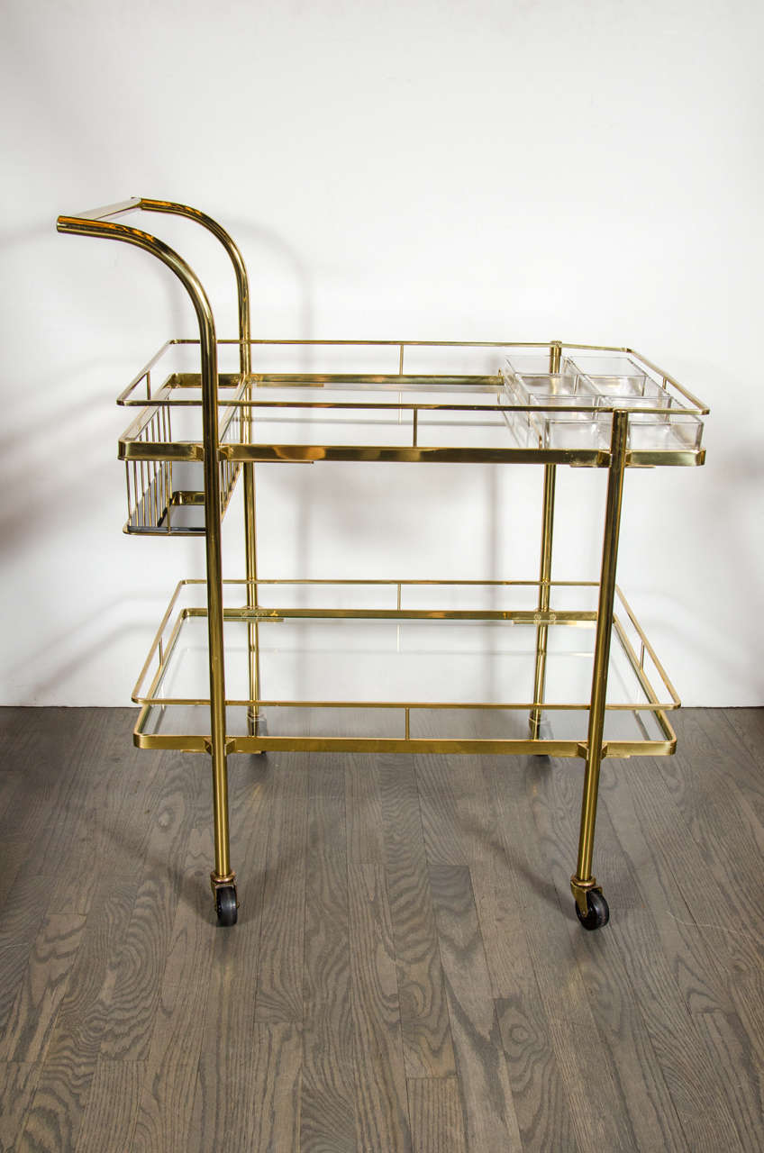 This chic Mid-Century Modern bar cart features a banded brass frame with a tubular brass handle, clear glass shelves, the top shelf has six removable glass partitions and a sunken bottle holder with vitrolite insert. This sturdy bar cart moves with