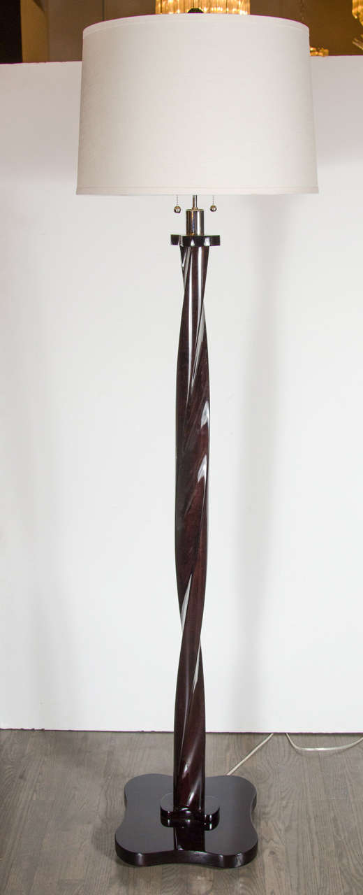 Mid-Century Modernist floor lamp in ebonized walnut with chrome fittings. This floor lamp features a twist formed thick stem that sits atop its clover shaped base. The stem is capped on top and bottom by a stylized bow-tie form adornment. It has