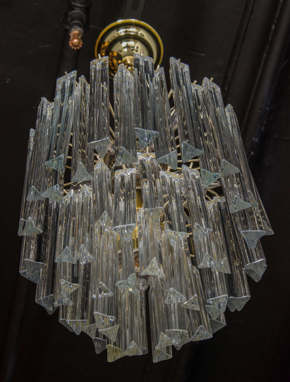This exceptional Mid-Century Modernist Camer chandelier features individually handblown Murano glass triedre prisms that hang from its polished brass frame in a cascading effect. The high quality glass reflects the light beautifully for added