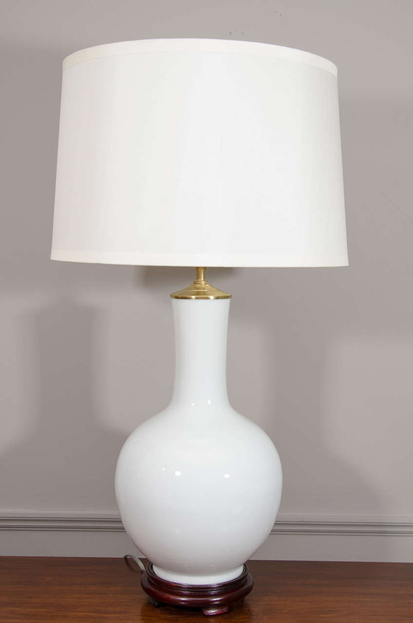 This pair of Chinese white porcelain vases, wired as lamps, are of the tianqiuping or globular form, first popularized during the Ming dynasty. Each is on a molded wooden base with a brass cap and light fixture, with a three-way switch. Shades