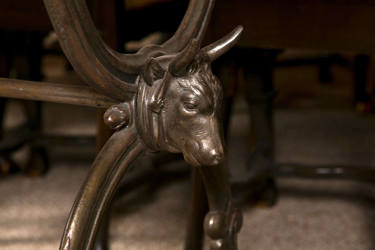 One-of-a-kind console table in the neoclassical style, circa 1950s, the beveled glass top supported on an iron base, each side decorated with bull's head, scrolled leg and stretcher.