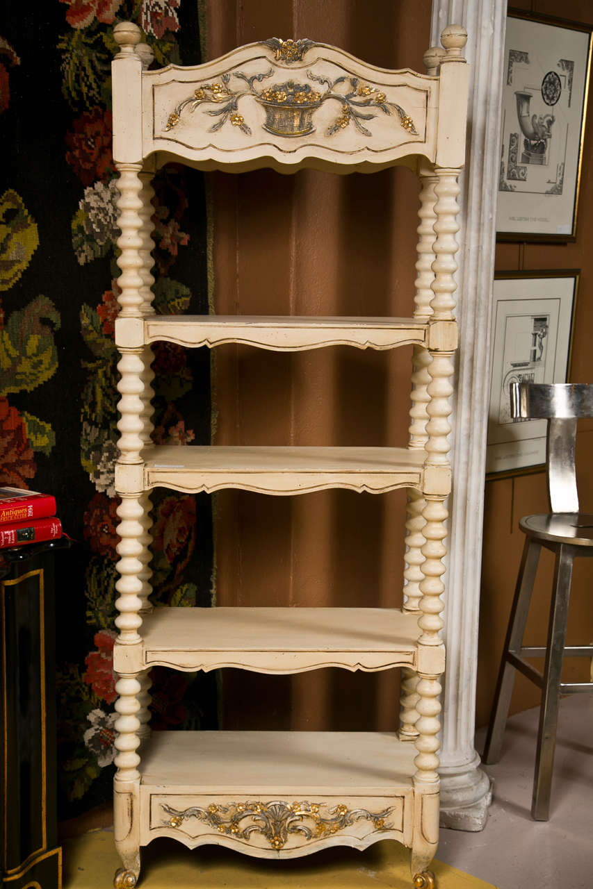 The pair of decorative ivory color painted etagere bookcases, 20th century, each has three tiers and bottom shelf supported by barley twist uprights, the bottom raised on scrolled toes.