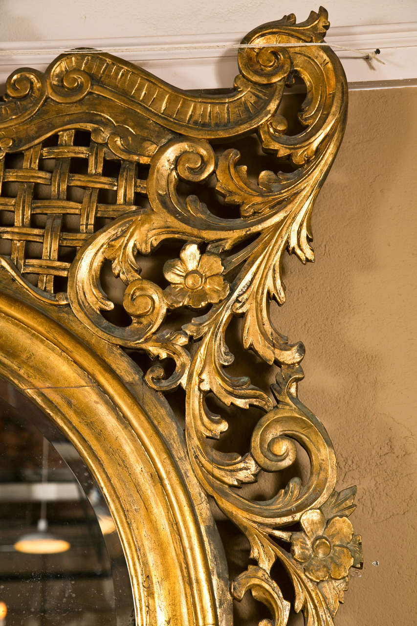 A spectacular French floor mirror in the Rococo taste and monumental in size, 3rd quarter of 19th century, overall gilded and naturally distressed in original finish, the domed mirror surmounted by intricate carving of scrolls, foliate, patera and