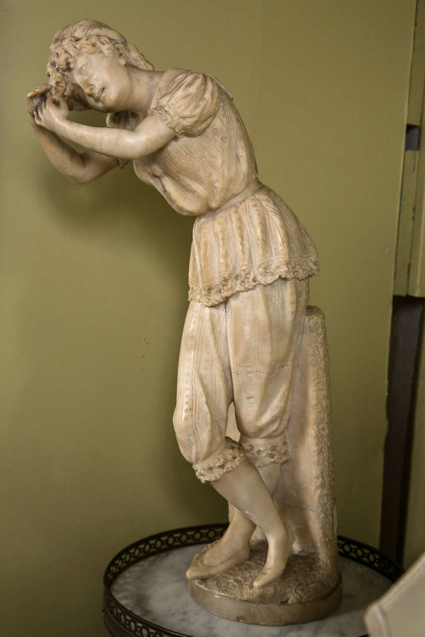 A nicely cast alabaster figure of a young woman in her pajamas washing out her hair. In 19th century attire this figure is leaning upon a slab of stone rinsing her hair out.