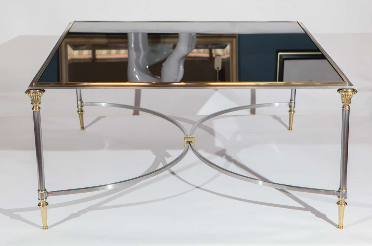 A vintage Hollywood Regency coffee table in the manner of Maison Jansen. Base is brass and brushed steel. Top is black mirror.