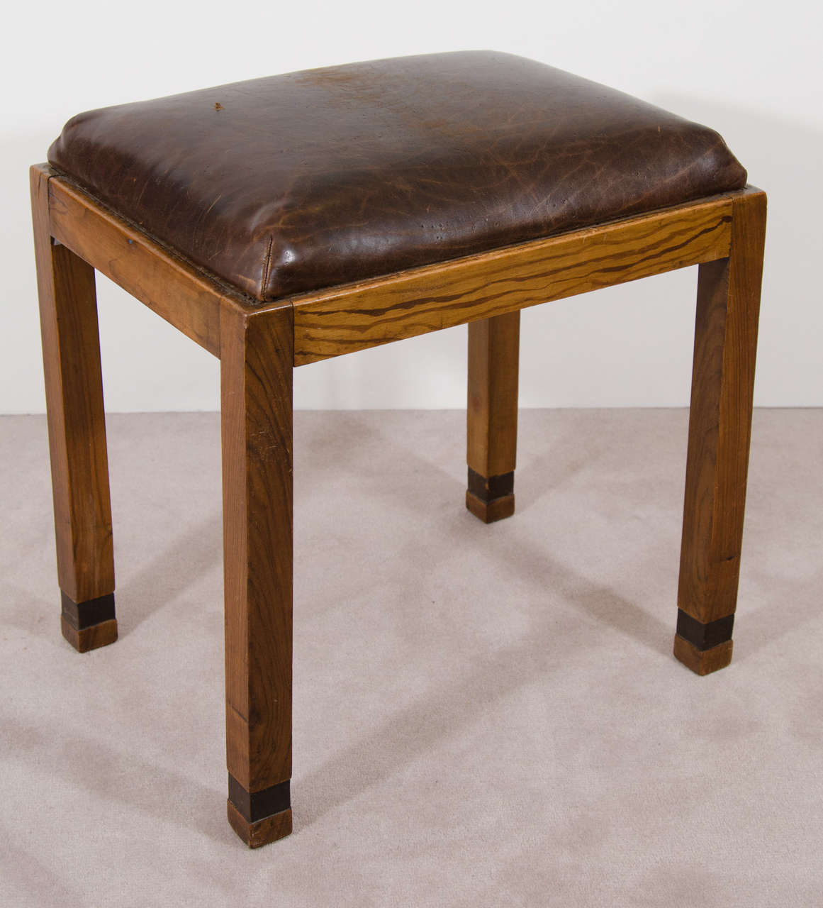 A handmade Folk Art stool in wood with brown leather seat.

Fair condition with scratches and nicks to the leather and wood. The underside has been reinforced with a new piece of plywood and corner blocks.