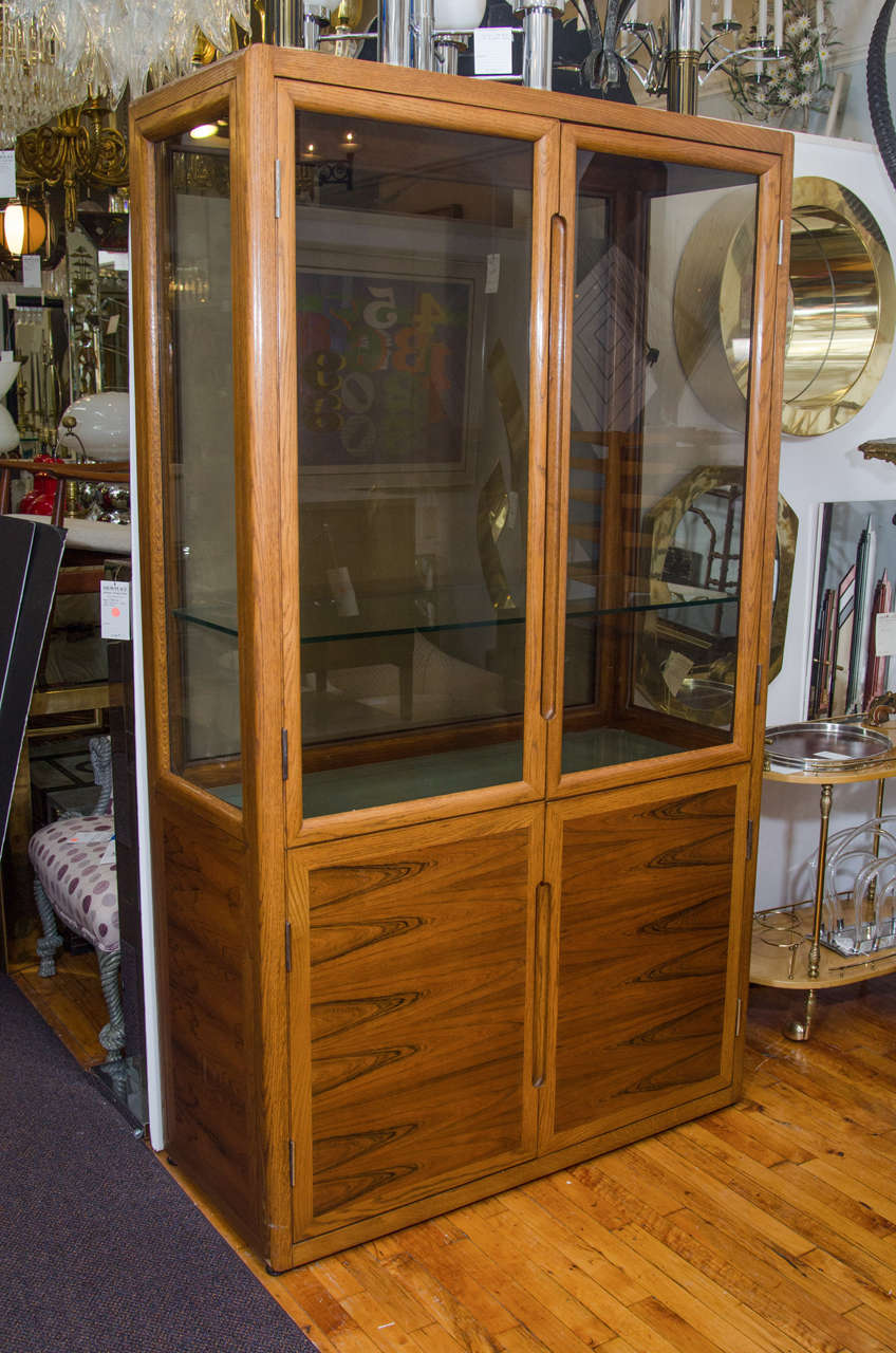 A vintage Dunbar double door wood and glass display cabinet with interior shelves.

Good vintage condition with age appropriate wear. There is a chip to one of the frosted glass shelves and some scuff marks and scratches to the wood on the outside