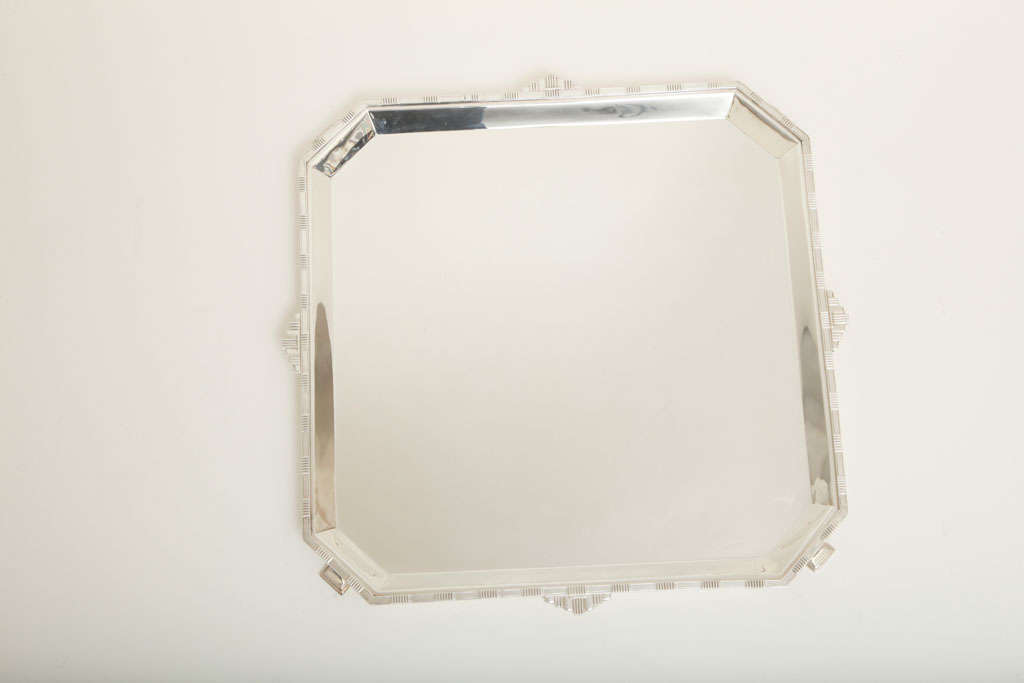 This square tray sits upon four stylized feet, has cut corner detailing and is decorated with a ribbed geometric pattern on the outer edge. It is very stylish and a great example of Art Deco design. It is in excellent condition. Marked 