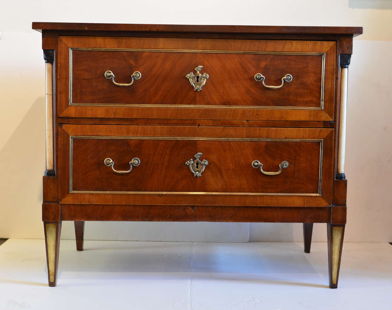 This exquisite Biedermeier German mahogany chest features a rectangular top over two banded and butterfly veneered drawers. Each drawer is a work of art on its own. The brass handles flank a lovely central escutcheon, depicting two cornucopias,