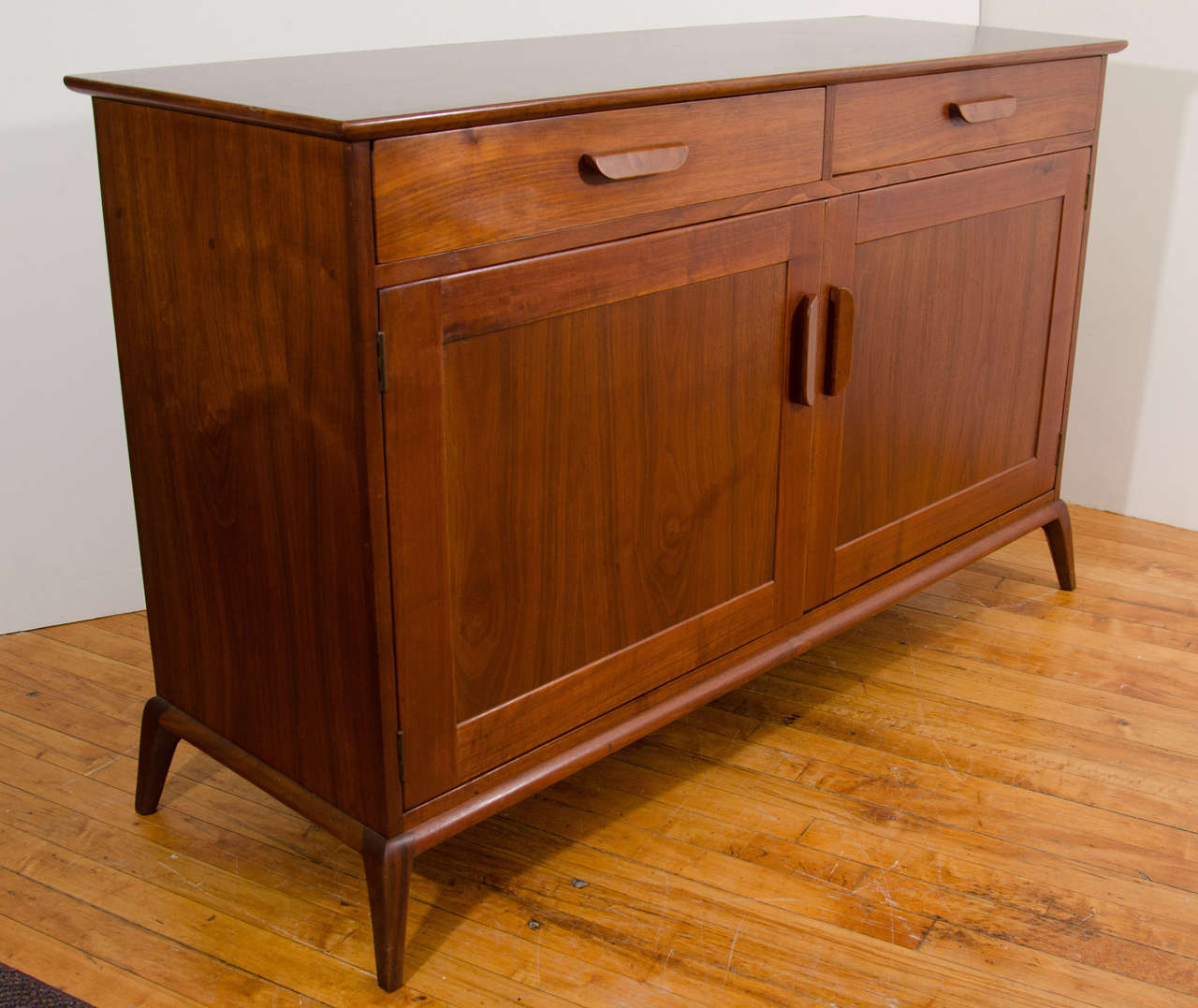 A vintage teak credenza or sideboard with two shallow drawers over a double-door cabinet. The interior has a narrow shelved space on the left and a large shelved space to the right.