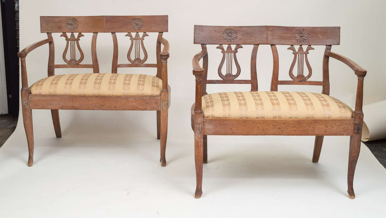 A pair of late 18th century Italian Neoclassic walnut benches. Lyre backs. Rosettes inlaid on the top backs and the legs. Hoof feet. Upholstered drop in seats with older brocade fabric. Small intimate size. Subtle lyme glazed (white) surface.