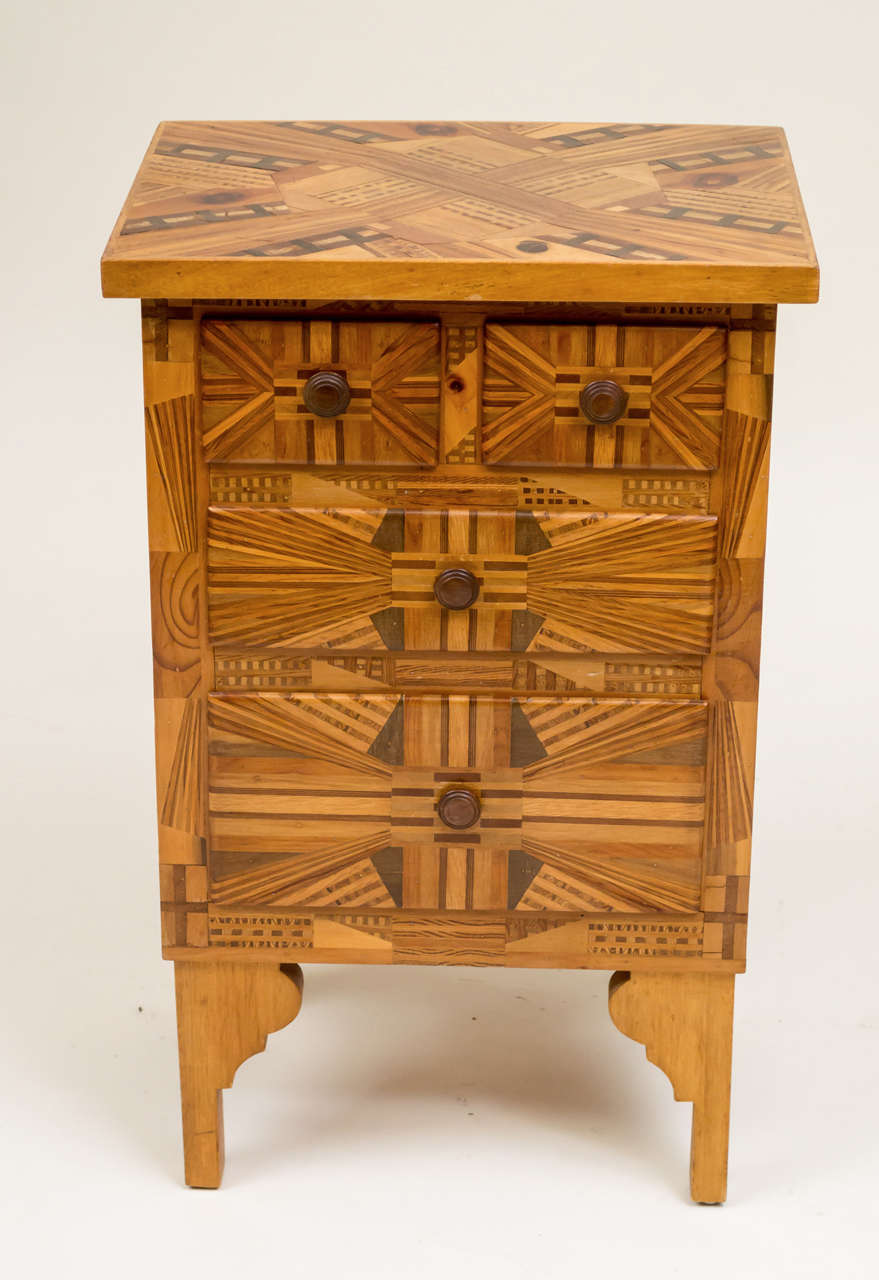 Early 20th century American Folk Art three-drawer side table. Made of thick laminates (over 1000) on all sides and the top. Supported on four tall bracket feet. Very intricate geometric marquetry. Individually hand-turned knobs.
