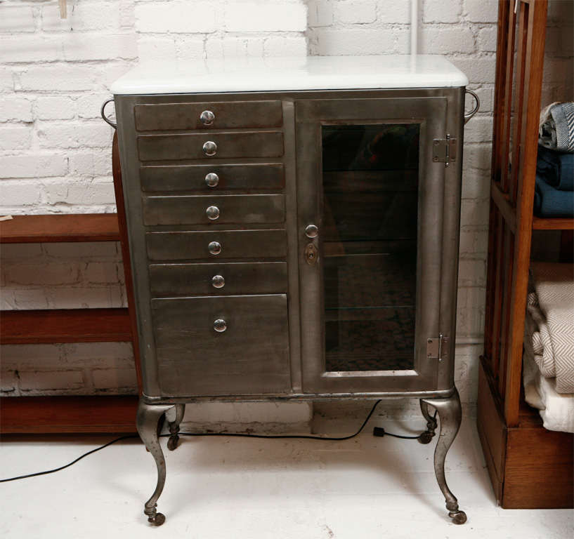 Classic stainless medical or dental cabinet.  Has white enamel top, six drawers,three glass shelves and a pullout bin.