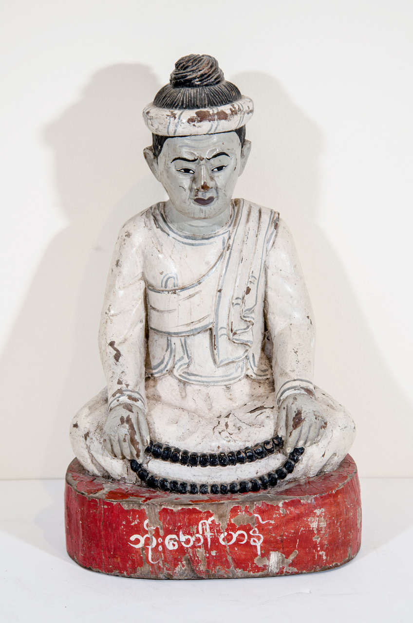 A beautifully carved and weathered seated monk holding prayer beads. This Burmese piece was donated to a Buddhist temple by the person named in the center of the red base.
BH432.