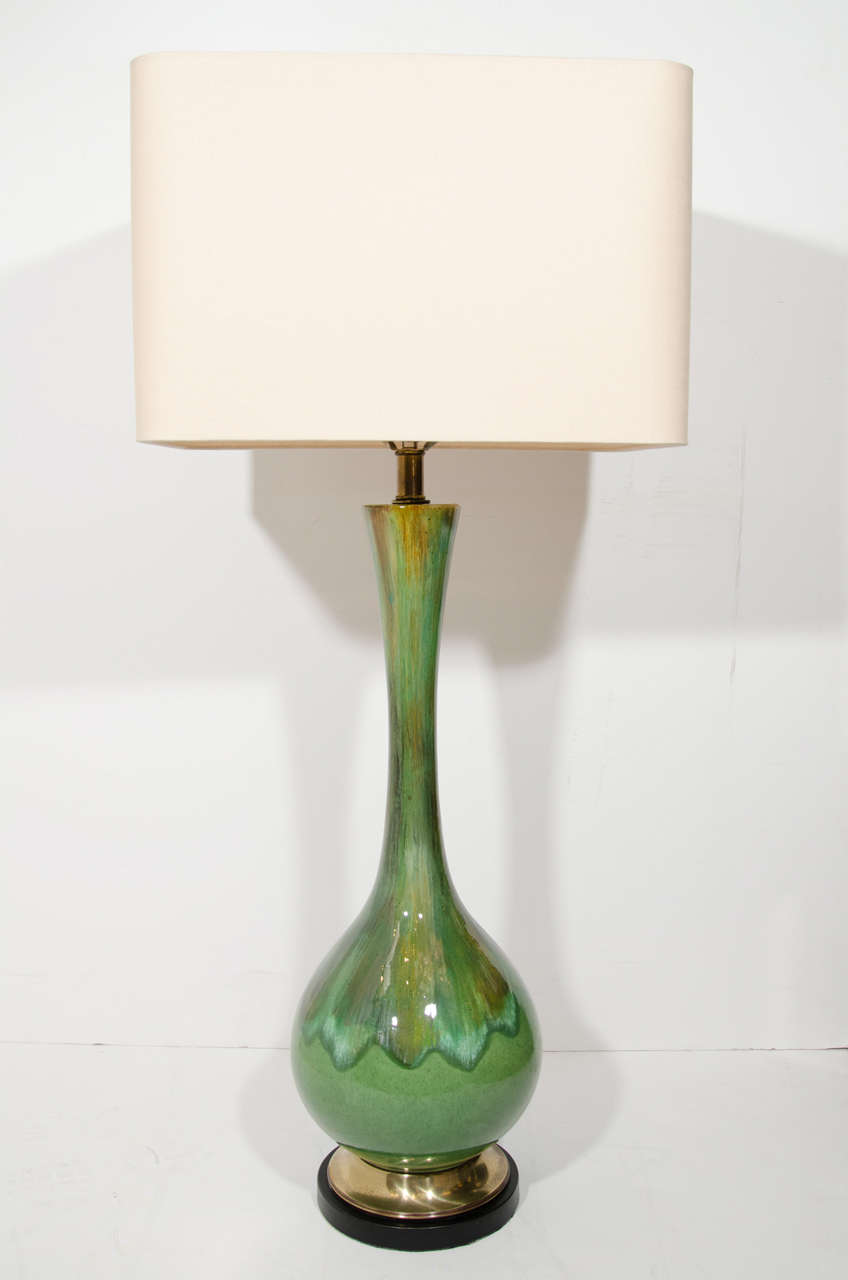 Pair of mid century modernist ceramic lamps with long neck design. The lamps have a drip glazed finish in variant hues of moss green and slight hints of moss brown. The lamps feature patinated brass stems and have brass fittings over black enameled