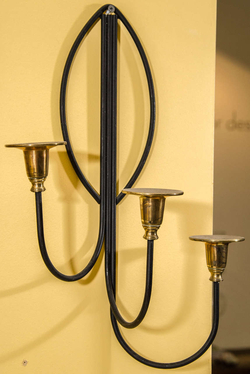 Graceful and pretty pair of candle wall sconces with wrought iron armatures and brass candle holders. 