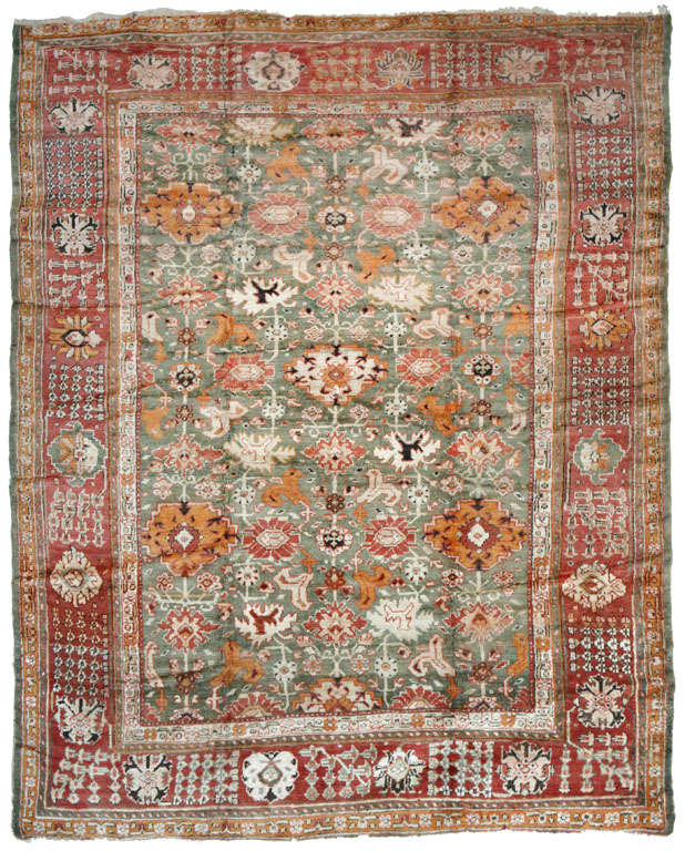 A sumptuous Oushak Turkish rug with an overflowing floral quality. Brick red, olive, orange, grey, brown, cream and ivory predominate. A border checkered blossom groupings and floral emblems encloses a field of large stemmed blossoms and stylized