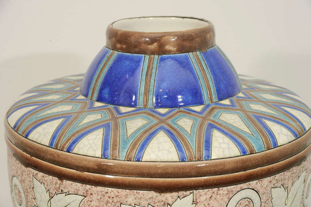 Blue glazed jug shape vase with glazed band of leaves on rough mottled white crackel background.