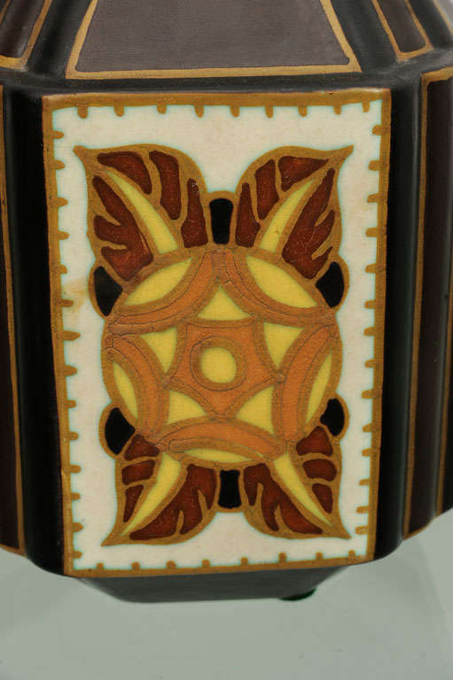 Four-sided brown ceramic vase with wide fluted corners and pyramid top and four yellow and Siena painted medallions on white background.