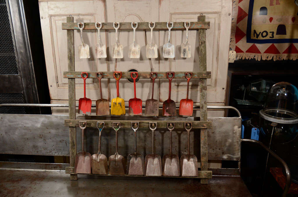 collection of 21 painted and unpainted metal shovels displayed on 3-tier wooden rack with pegs