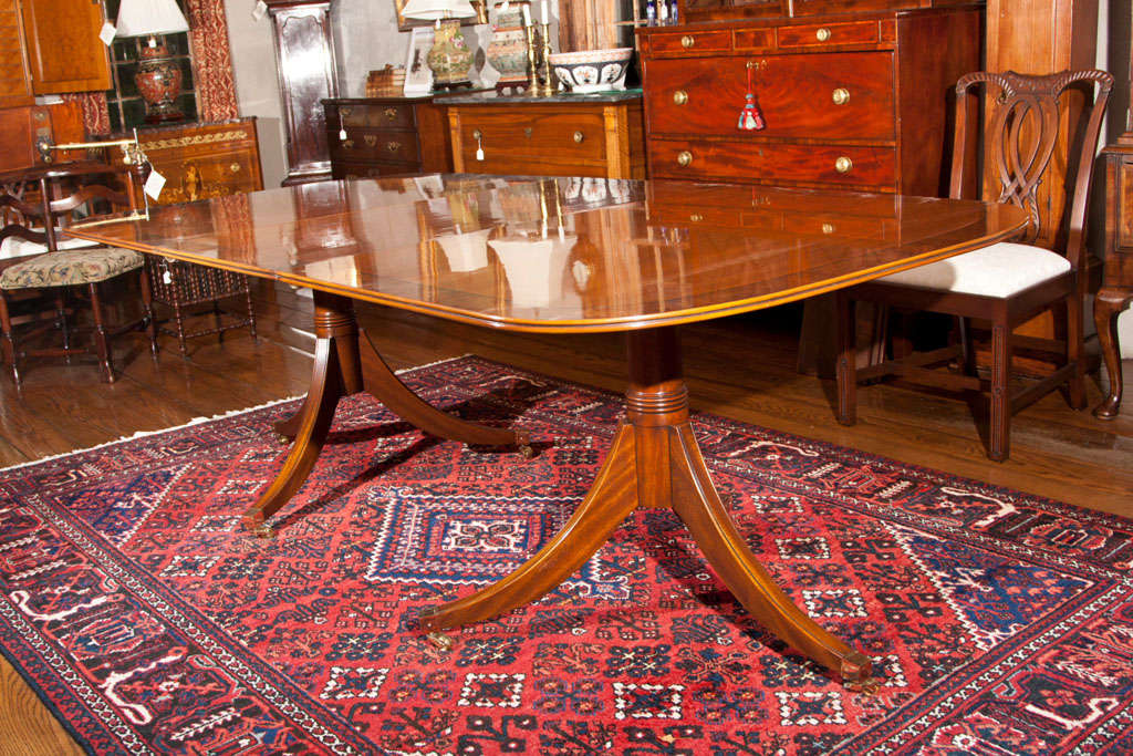 Custom made, English walnut double pedestal dining table. This richly finished table features a handsomely figured English walnut top bordered in walnut burl, and it rests on two three-leg, turned column pedestals with brass toe caps and casters.