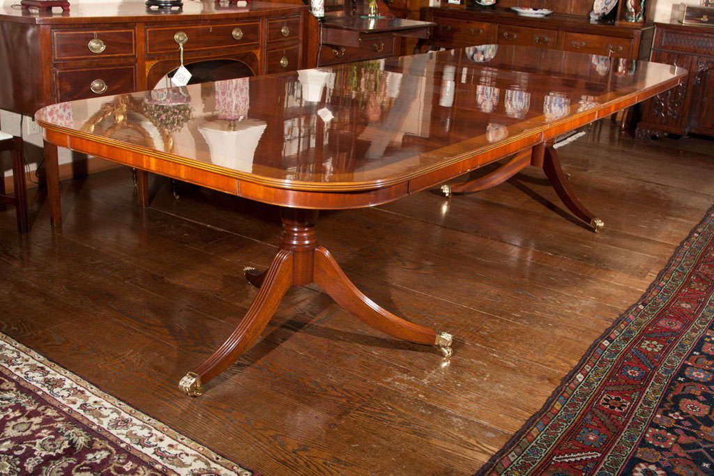 Double pedestal, flame mahogany dining table with satinwood crossbanding, beaded edge, mahogany apron. Cannon turned single column pedestals with reeded legs ending in brass 