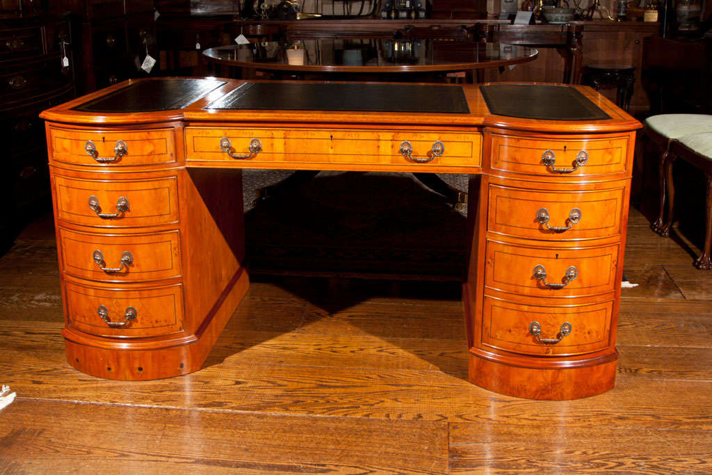 Three part, English yew wood modified partners desk with uniquely shaped top and pedestals. File drawer to one pedestal, graduated drawers to the other. Opposite side has three drawers across top and each pedestal has a small cupboard with false