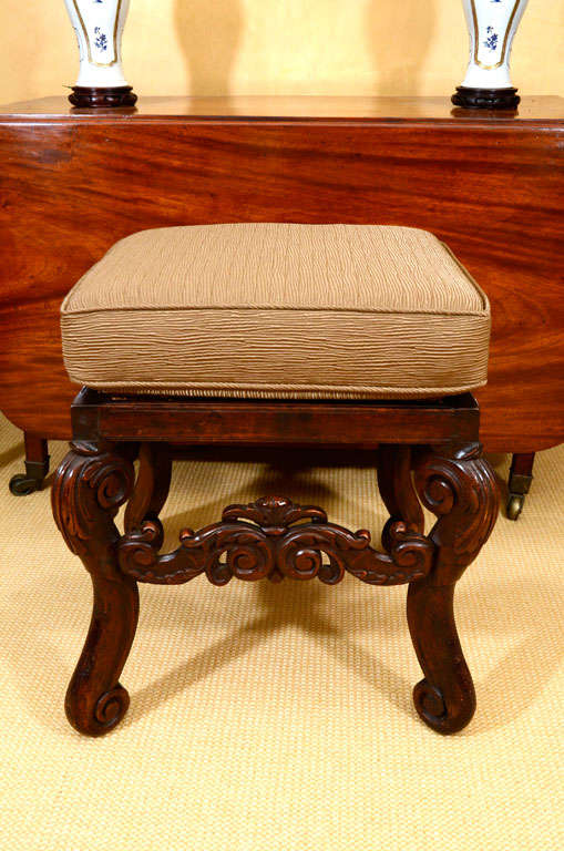A very highly carved walnut stool with caned seat and cushion