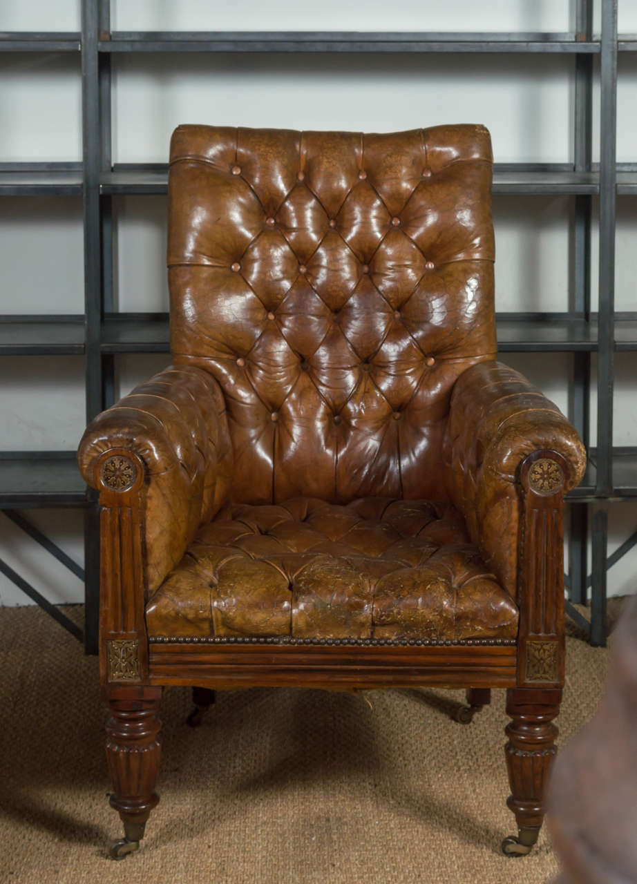 Mid Century tufted brown leather club chair on wheels. With ornate carvings on the wood base around the arms and legs.
