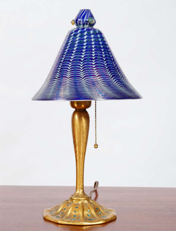A Tiffany Studios lamp. features a favrile glass shade in blue and white with iridescent accents, held by a bronze base with enameled accents and an original gold dore patina. Shade signed L.C.T. Favrile, base signed Louis C. Tiffany Furnaces. Shade