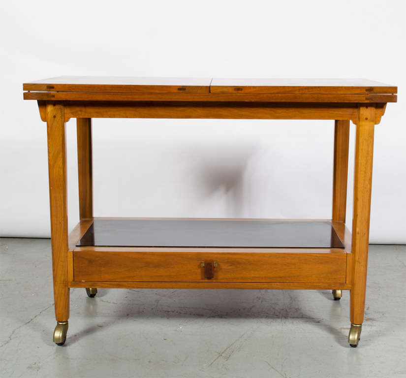 A bar cart made of walnut and mahogany with a formica shelf and brass wheels.

Signed with applied gold rectangular manufacturer's label to drawer: [Dunbar Berne, Indiana].

Literature: Dunbar Furniture Corp. of Berne, Indiana: Edward J. Wormley