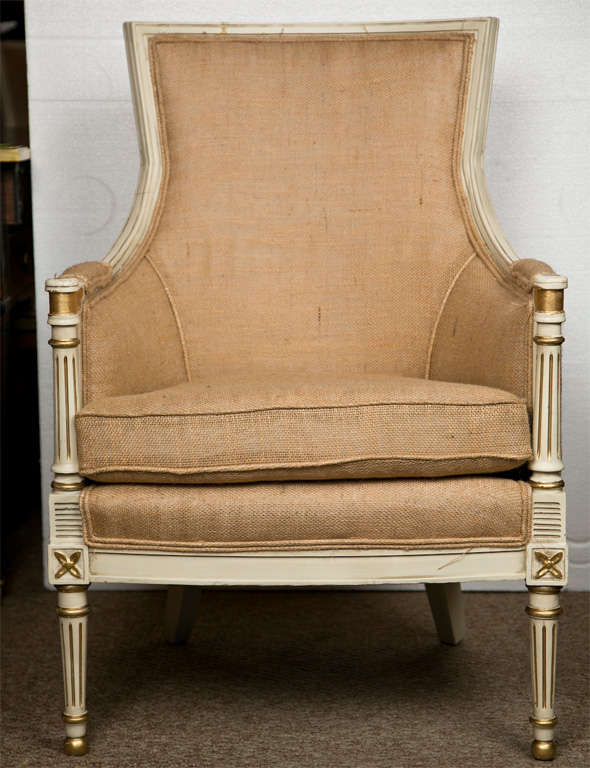 Pair of French Louis XVI style creme peinte bergere chairs, circa 1940s, parcel-gilt on frame, padded back and arms, cushioned seat, upholstered in burlap. By Jansen.