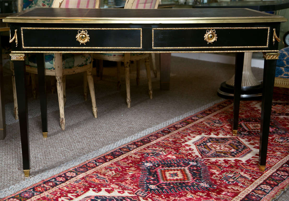 Beautiful French Directoire style writing table or desk, circa 1940s, overall ebonized, the embossed leather writing surface with ormolu banding atop a narrow frieze fitted with two drawers, each with bronze banding and loop pulls, raised on squared