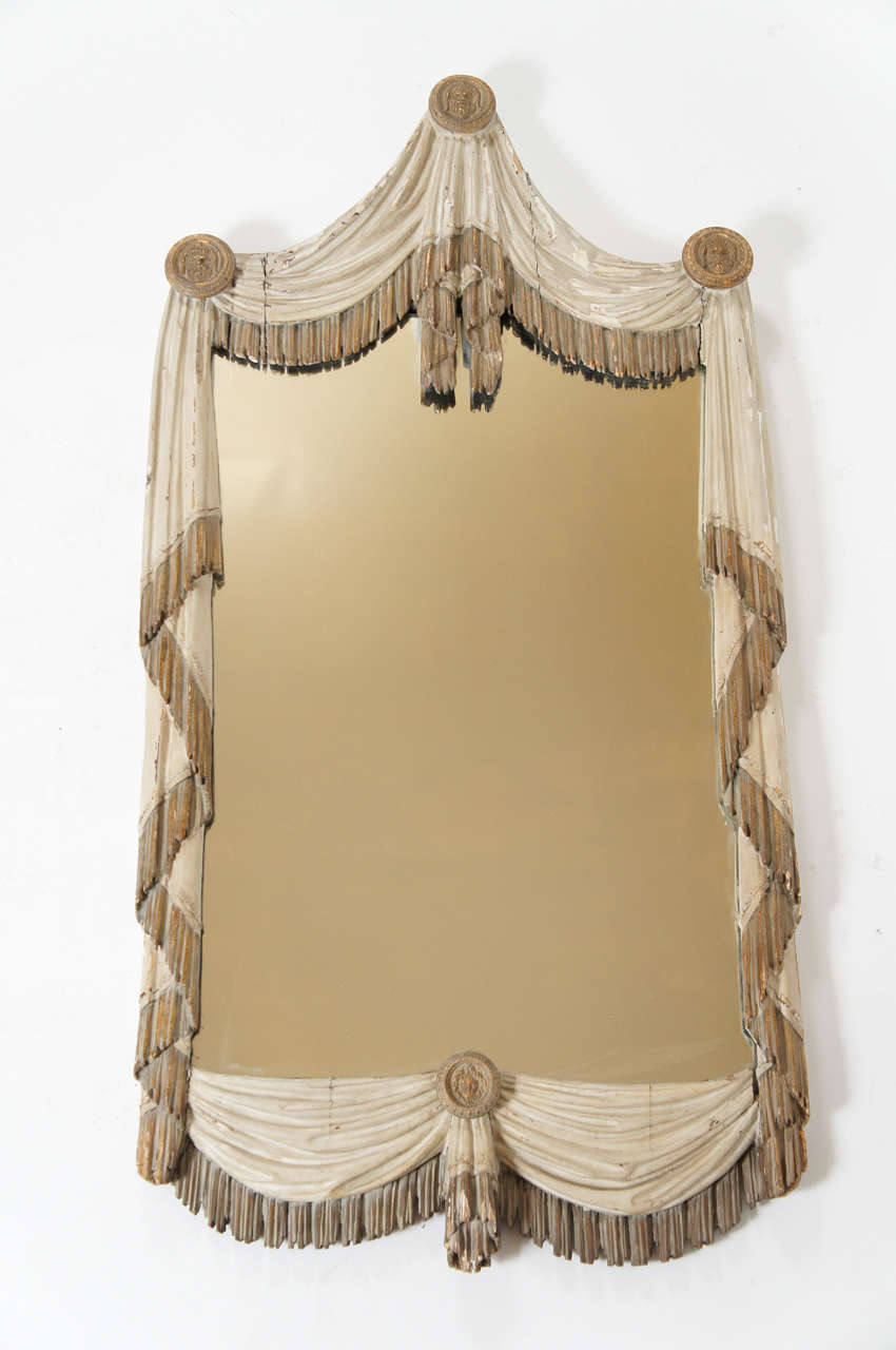 Rare and exquisite Italian circa 1800 looking glass having realistically carved gathered and tasseled drapery motif frame with carved and gilt wood mask roundel 'tie-backs'. Original unrestored painted and gilt finish. Exceptional piece.