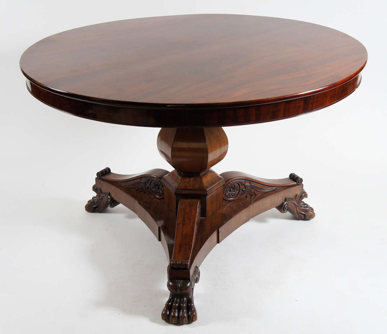 Exquisite large round center table of pedestal form having corresponding top on faceted baluster form center support surmounting elaborately carved tripod base having horizontal acanthus corbels ending in exceptionally detailed lion's paw feet.  A