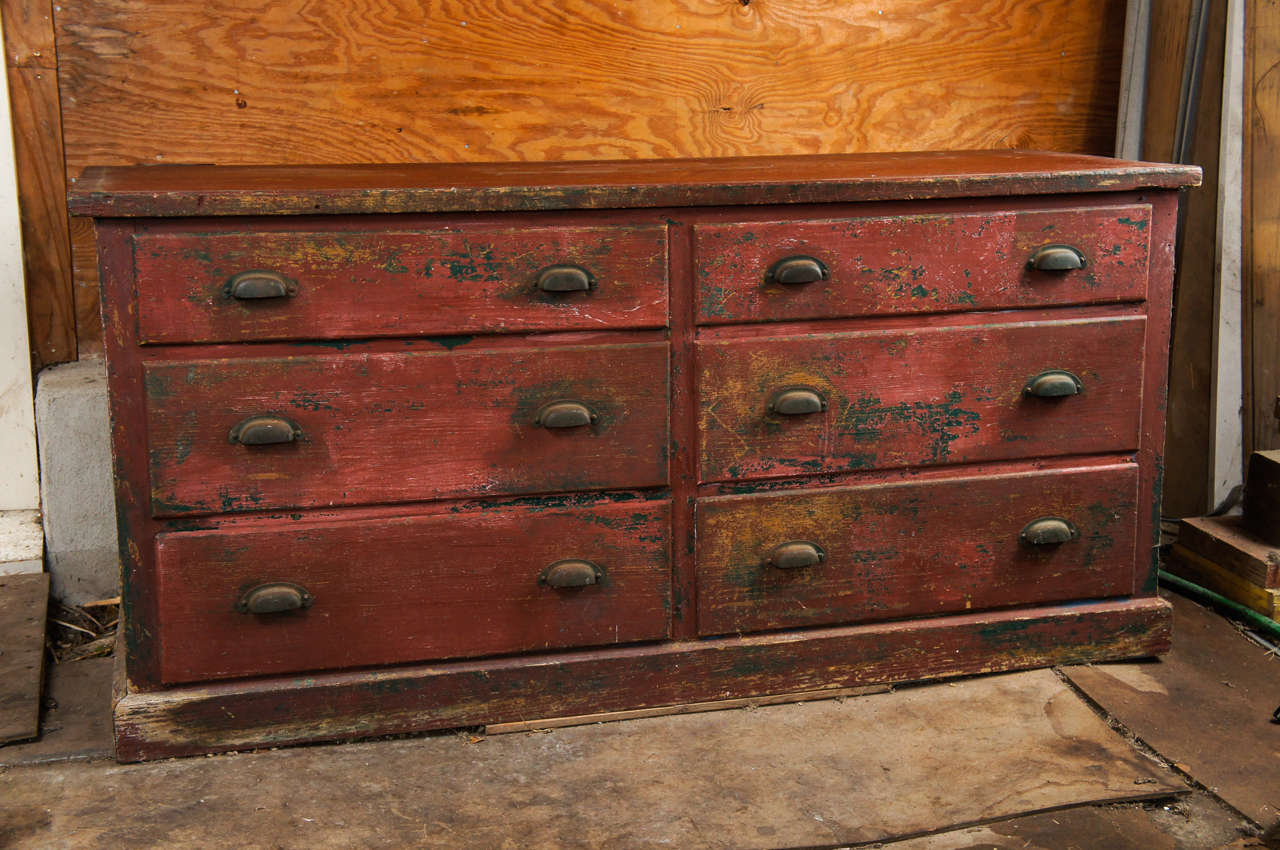 Turn-of-the-last-century, handmade chest of drawers with exposed layers of red and green milk paint and original brass handles.