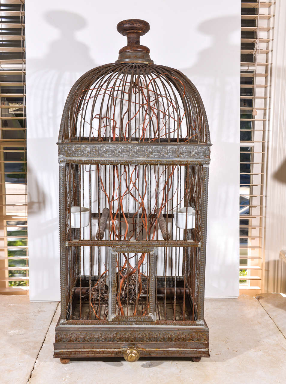 This is a beautiful and functional bird chateau with pull-out enameled floor liner and porcelain feeding stations, as well as three wood perches and a swing. It is currently displayed with branches and a nest on the interior.