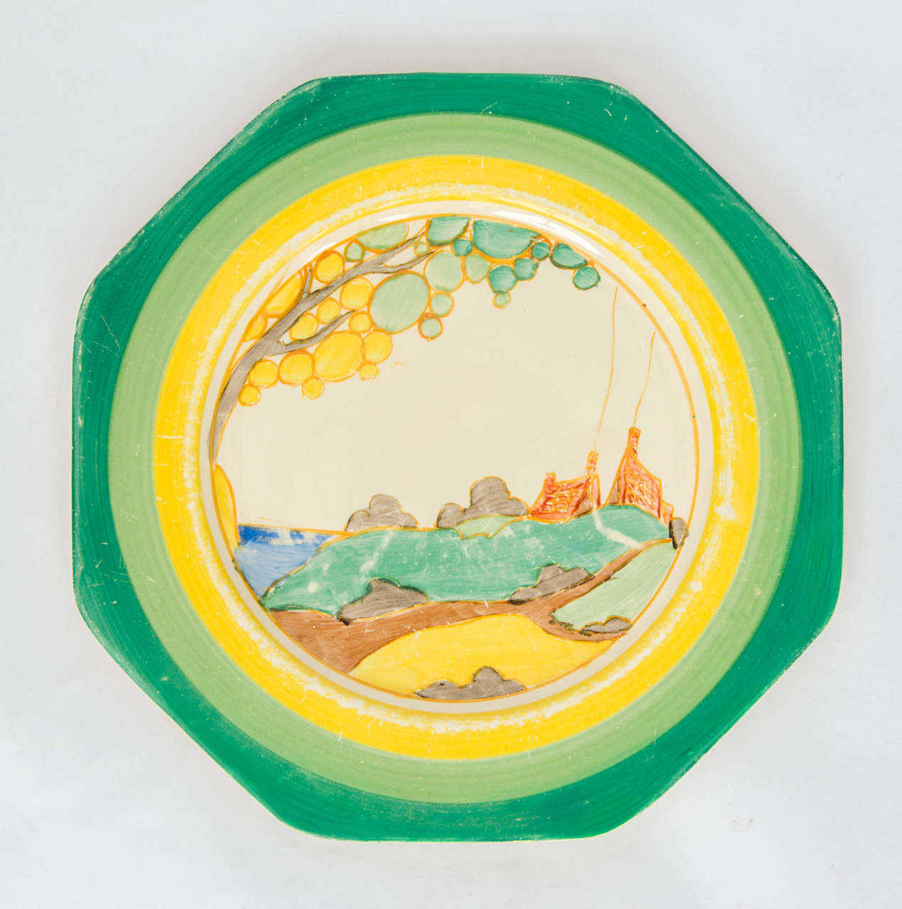 This is a hand-painted Clarice Cliff plate in the classic landscape Bizarre pattern called; Secrets.

The plate is octagonal and has the two-tone green and yellow banding color way (there was a later version with orange banding).

The plate is