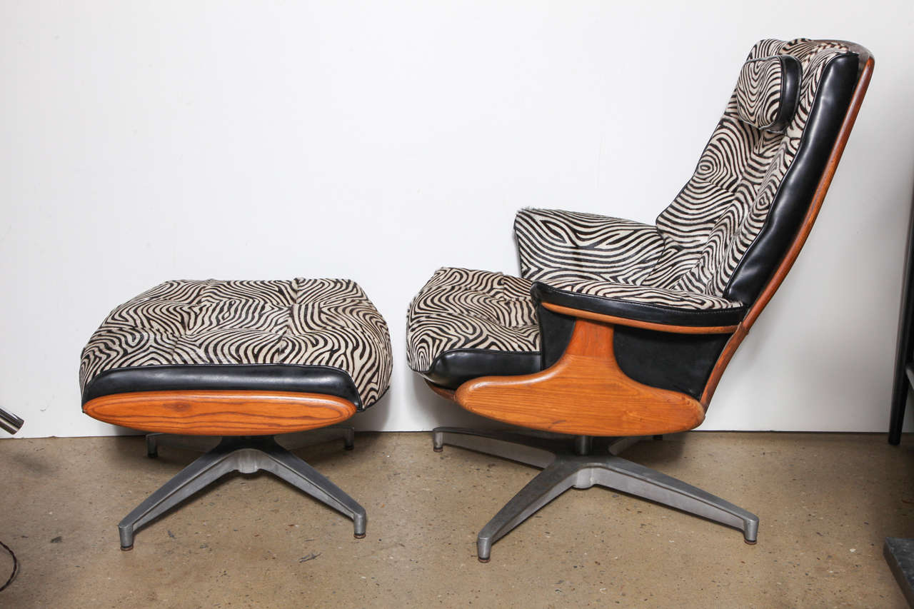 late 1960's ergonomic Heywood Wakefield reclining spring back Lounge Chair and Ottoman in the manner of the famous Eames 670 design. This Maple stained Oak Chair and Ottoman is seated on an open 4 legged Cast Aluminum swivel base. Custom upholstered