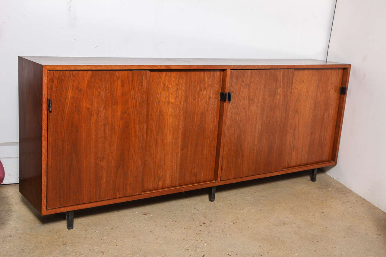 early 1960's Florence Knoll designed slender Walnut Bookcase Crendenza, Buffet or Cabinet with original Black Leather tab handles seated on 6 Black Metal square legs with 2 sliding doors and 4 interior shelves.  Original finish.  Ideal for large 60