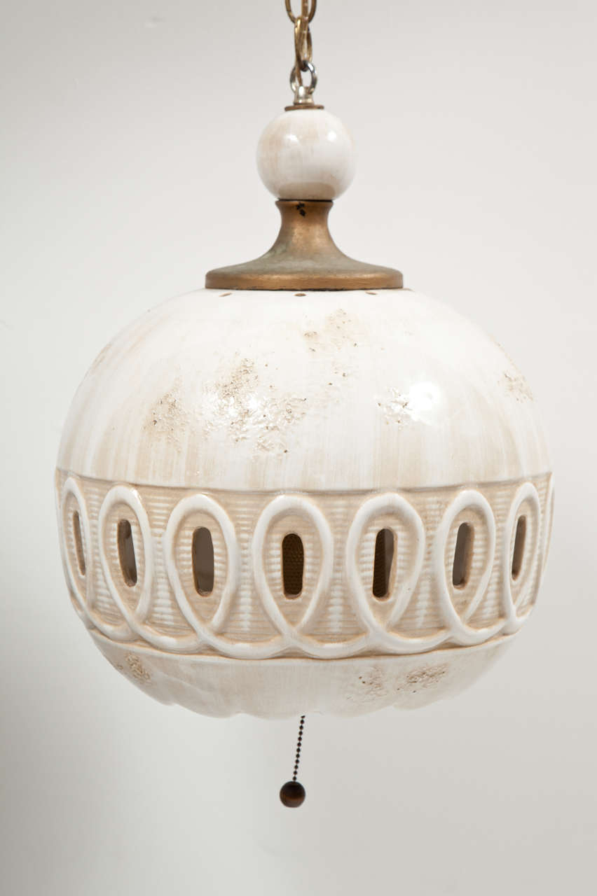 Bone-white ceramic pendant light fixture, possibly by Georges Pelletier.  France, circa 1950.  Unsigned.  Features perforated detailing and an interior brass diffuser. Creates beautiful light effect when lit. Includes hanging chain and on/off pull